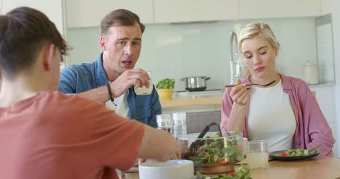 Family sharing casual lunch at kitchen table, dad talking while teen reaching for salad