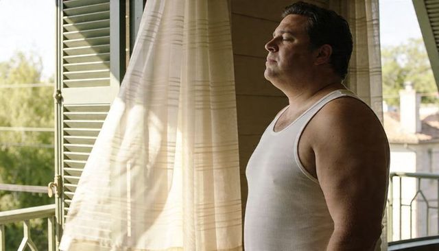 Man standing at open french window with billowing curtain, basking in morning light