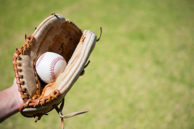 Cropped hand of baseball pitcher holding ball in glove at field