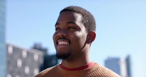 African american man smiling on rooftop with urban skyline sunlit portrait