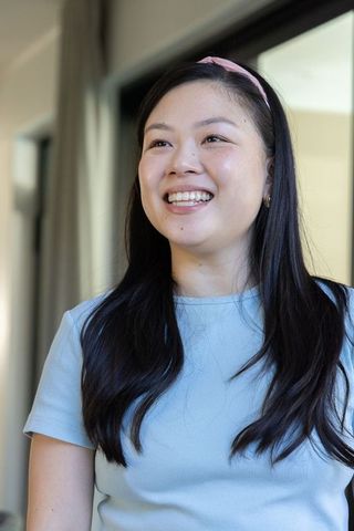 Asian woman smiling and looking up near glass door wearing pink headband, blue top