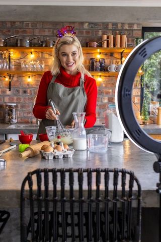 Female baker whisking batter on rustic kitchen island while recording with ring light