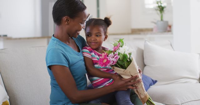 Mother receiving bouquet of flowers from young daughter in bright living room. Scene is filled with love, happiness, and family bonding. Perfect for Mother's Day promotions, family-oriented content, and parenting articles.