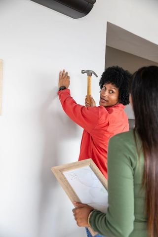 Young Couple Collaborating on Home Decor Project with Hammer and Frame