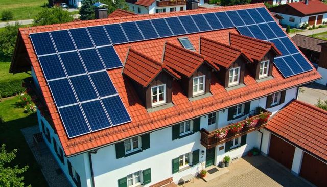 Two-story alpine house with photovoltaic solar panels on red tile roof and flower-filled balcony