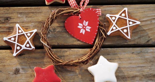 A rustic wooden background features a variety of festive Christmas decorations, including a heart-shaped wreath and star-shaped cookies. These holiday ornaments and treats create a warm, inviting atmosphere, evoking the cozy spirit of the season.
