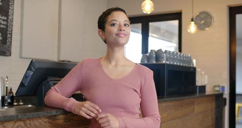 Confident barista welcoming customers at cafe counter using touchscreen pos with espresso