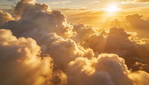 Sunlit golden cumulus clouds soaring above horizon with dramatic sunbeams