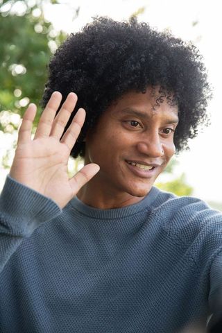 Smiling man waving outdoors in casual attire