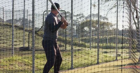 Batter Practicing Swing in Outdoor Batting Cage with Protective Netting and Sunlight