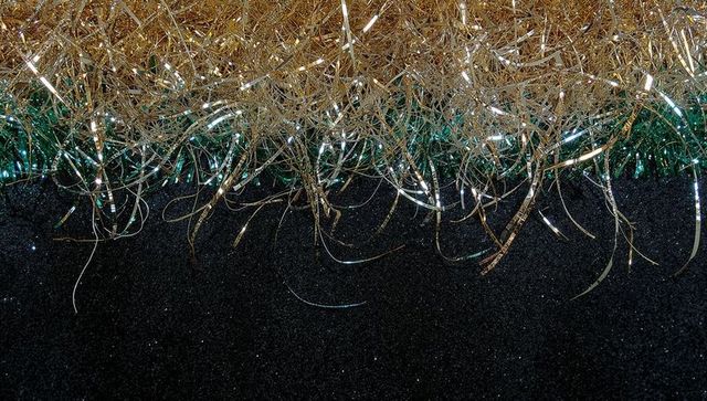 Gold and green tinsel garland shimmering over dark sparkling surface with silver filaments