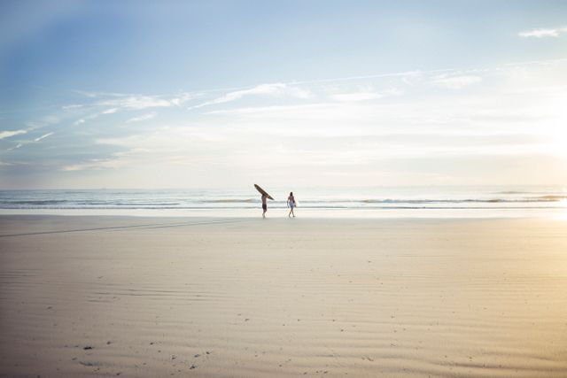 Individuals carrying surfboards taking an early morning walk along a sandy beach. Ideal for promoting travel, summer vacations, outdoor activities, and water sports.