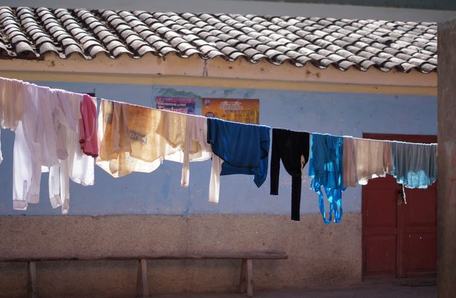 Clothes in various colors drying on a line outside a rustic house with a weathered wall and red door, typical of a rural village. Perfect for content about traditional lifestyles, countryside living, and drying laundry outdoors. Useful for illustrating topics related to environmentally friendly practices, cultural backgrounds, or daily life in rural areas.