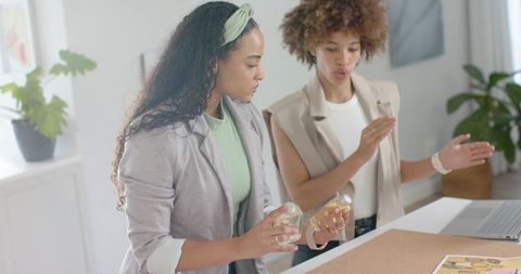African american women collaborating over clear bottle product samples at studio table