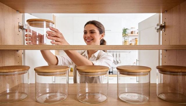Smiling woman organizing modern white kitchen pantry with glass jars and bamboo lids