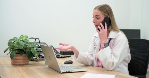 Female doctor talking on phone and using laptop for telemedicine consultation