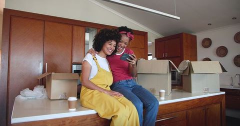 Joyful Female Couple Enjoying Smartphone Moments on Kitchen Counter