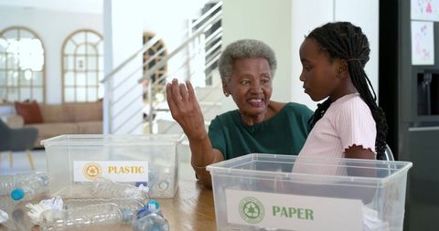 Grandmother Teaching Granddaughter Recycling at Home Sorting Plastic and Paper Bins