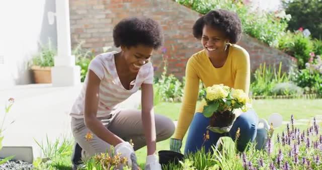 Smiling mother and daughter enjoying gardening on a sunny day provides a heartwarming example of family bonding. They collaborate while planting flowers, symbolizing teamwork and love for nature. This can be used in advertisements for gardening products, family lifestyle articles, or inspirational content about spending quality time with loved ones.