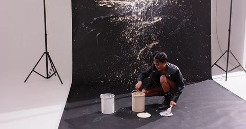 Studio artist stirring beige paint on black backdrop creating dynamic splash and motion