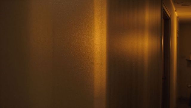 Moody amber hallway light casting textured wall reflections, corner shadow bands