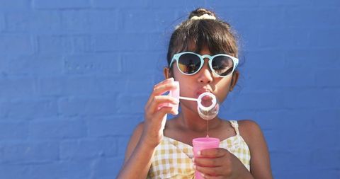 Young Girl Blowing Bubbles in Sunglasses Against Blue Background - Download Free Stock Images Pikwizard.com