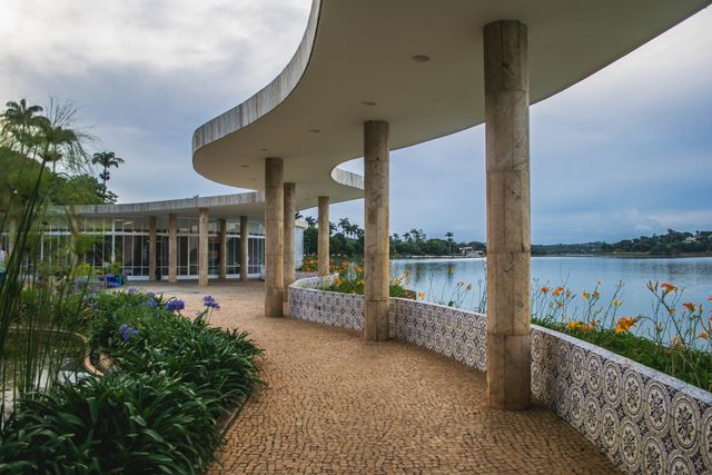 Scenic Pathway Along Calm Lake with Modern Architecture and Floral Garden - Download Free Stock Photos Pikwizard.com