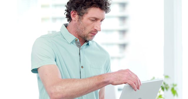 Mature man focusing while using a laptop in a modern office environment. Ideal for depicting professional work settings, business, technology usage, and office life.