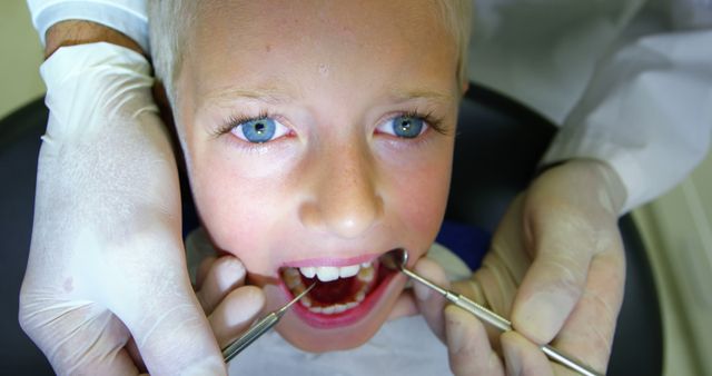 Boy sitting in a dental chair receiving a dental checkup with dental tools. Dentist using gloved hands to examine child's teeth. Perfect for dental care websites, pediatric dentistry promotions, health and medical campaigns, and educational materials on dental hygiene for children.