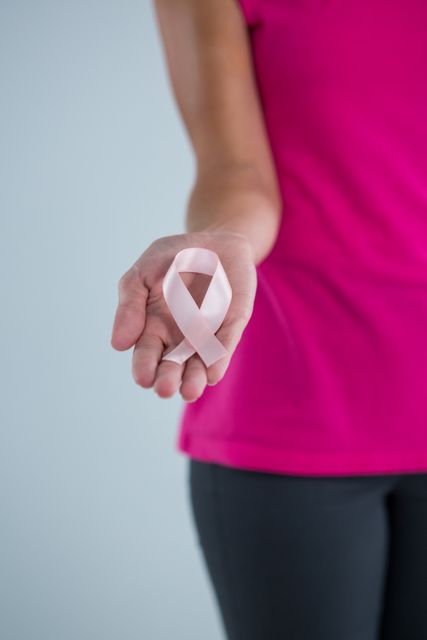 Mid section of female holding pink ribbon while standing against gray background
