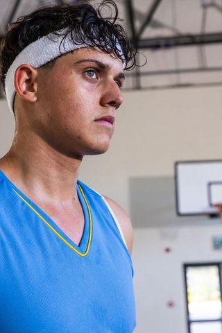 Focused up-and-coming basketball player in athletic uniform near court