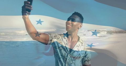 Smiling man taking selfie on sunny beach with honduran flag overlay
