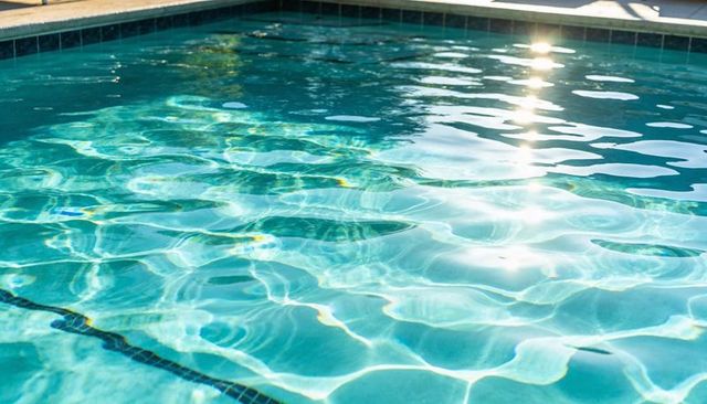 Glinting pool water rippling under sunlight with caustics and dark tile line on deck