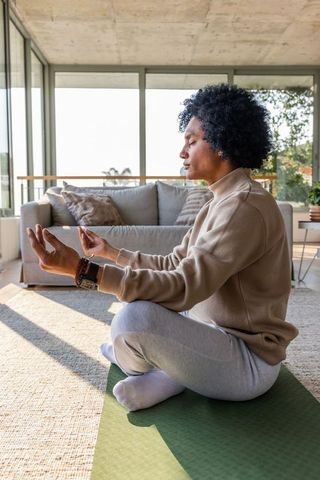 African american man meditating cross-legged on yoga mat in sunlit modern living room