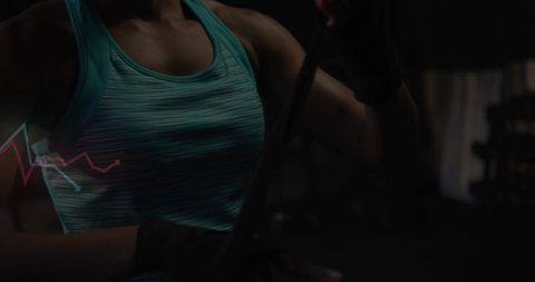 Adjusting boxing hand wraps in low-light gym wearing teal striped tank top, workout focus