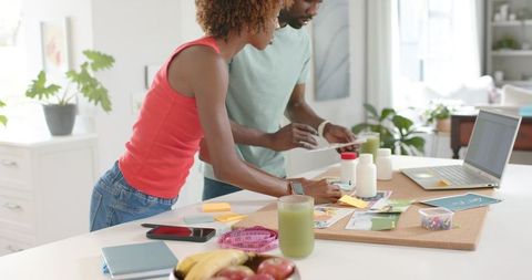Young couple collaborating on home project at bright kitchen island with laptop, corkboard