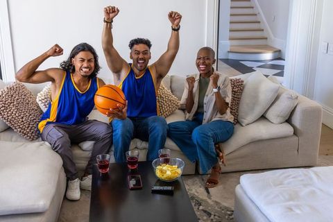 African american friends cheering together on sofa watching basketball game holding ball