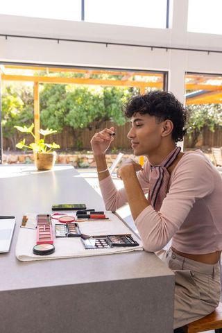 Young Man Applying Mascara in Bright Kitchen with Makeup Accessories