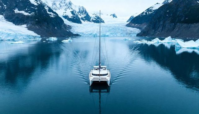 Catamaran cruising toward glacier in tranquil fjord with icebergs and mountain reflections