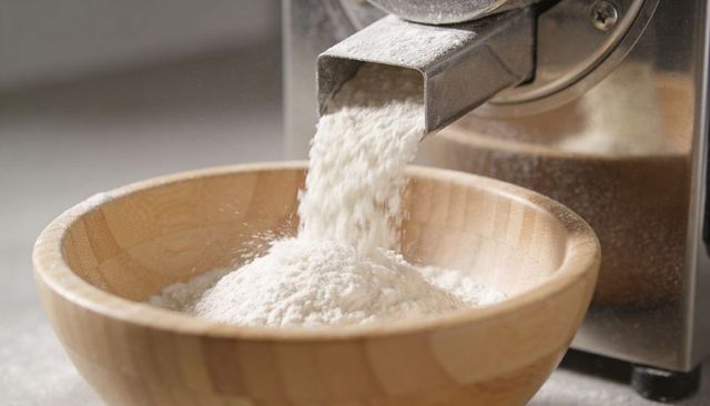 Pouring flour into wooden mixing bowl from stainless steel chute, close-up baking mill
