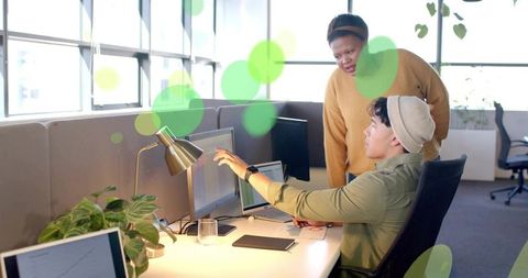 Colleagues collaborating at dual monitors in bright openplan office, pointing, reviewing work