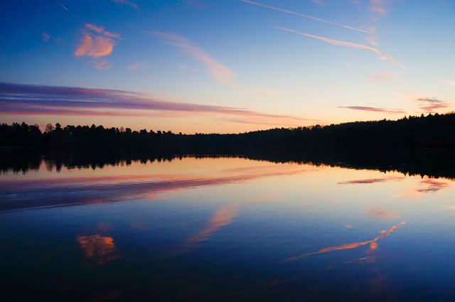 Perfect for backgrounds, travel brochures, nature documentaries, relaxation websites, and environmental campaigns. This serene scene captures a sunset over a calm lake with vibrant reflections in the water, emphasizing tranquility and the beauty of nature.