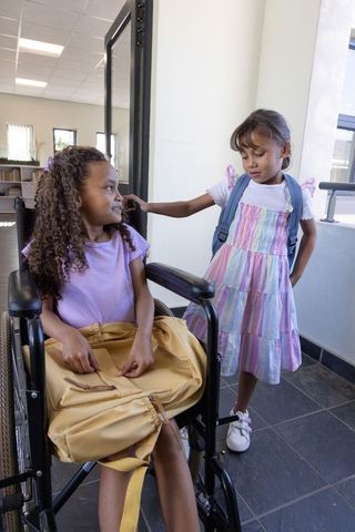 Diverse schoolgirls chatting at classroom door, wheelchair inclusion and back-to-school friendship