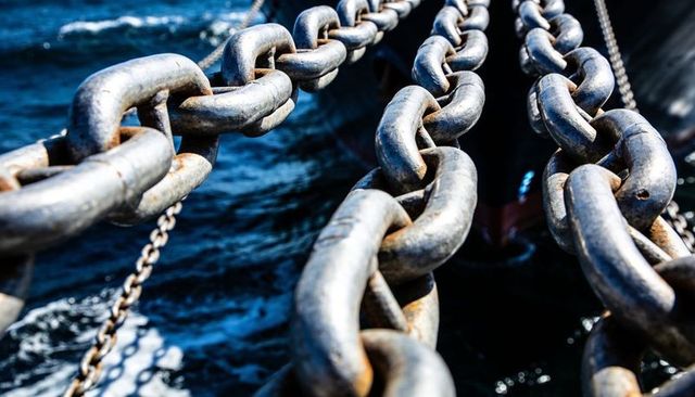 Hanging heavy mooring chains over deep blue sea showing weathered hull and rust texture