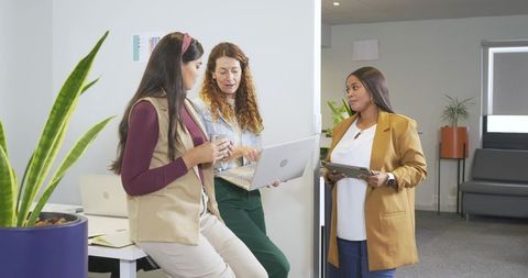 Diverse women collaborating in modern office with laptop and tablet, casual business attire
