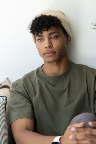 Young african american man sitting on sofa, clasping hands, wearing beanie and smartwatch