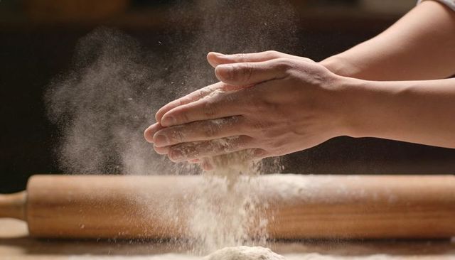 Hands dusting flour over dough with rolling pin closeup for baking content