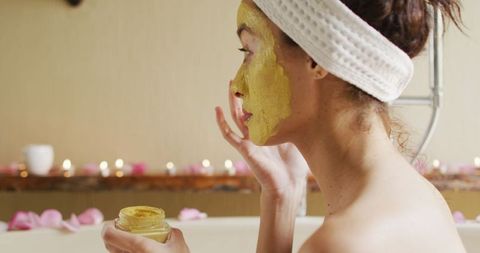 Woman with vitiligo applying face mask in relaxing home spa
