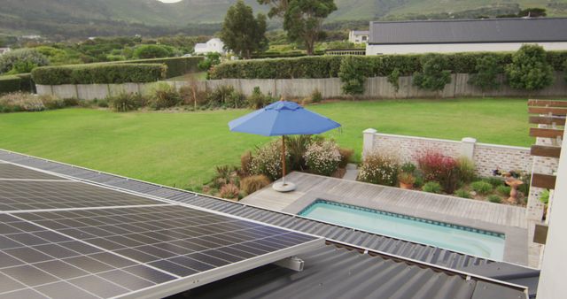 Overhead perspective showcasing solar panels installed on a rooftop, casting over a well-maintained backyard with a swimming pool, green lawn, and mountains in the backdrop. Ideal for content related to sustainable living, renewable energy solutions, and outdoor lifestyle.