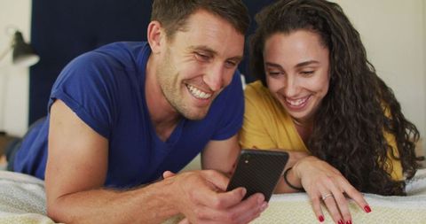 Cheerful Couple Relaxing on Bed Using Smartphone at Home